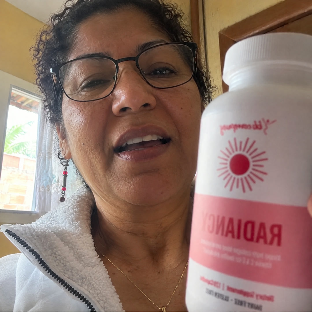 Mulher de cabelo curto e óculos segurando um frasco branco com rótulo rosa onde se lê "RADIANCY".